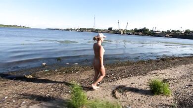 An exhibitionist girl walks on the river where there are ships and barges