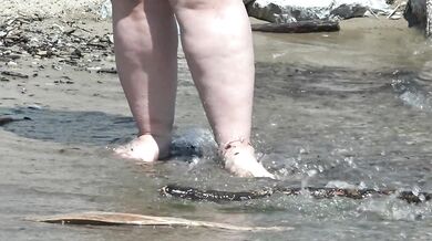 Fat bare legs with red pedicure walk along the bank of the river, fetish.