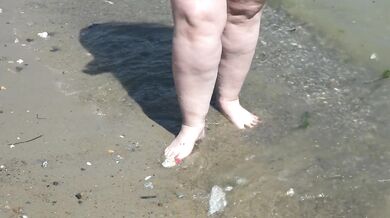 Fat bare legs with red pedicure walk along the bank of the river, fetish.