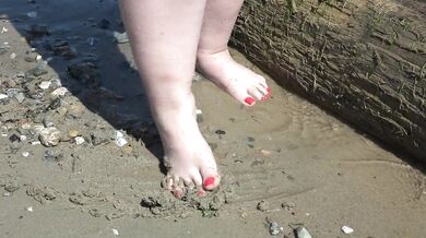Fat bare legs with red pedicure walk along the bank of the river, fetish.