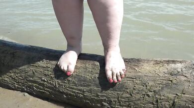 Fat bare legs with red pedicure walk along the bank of the river, fetish.