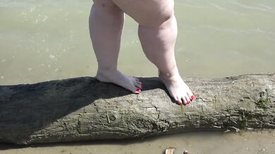Fat bare legs with red pedicure walk along the bank of the river, fetish.